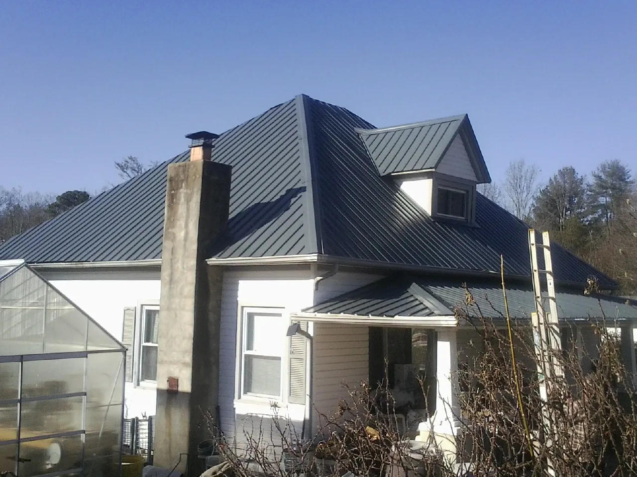 Dark blue standing seam metal roof on a white farmhouse with dormer — Slate & Tile Roof Repair by Roofing Brothers in State Center