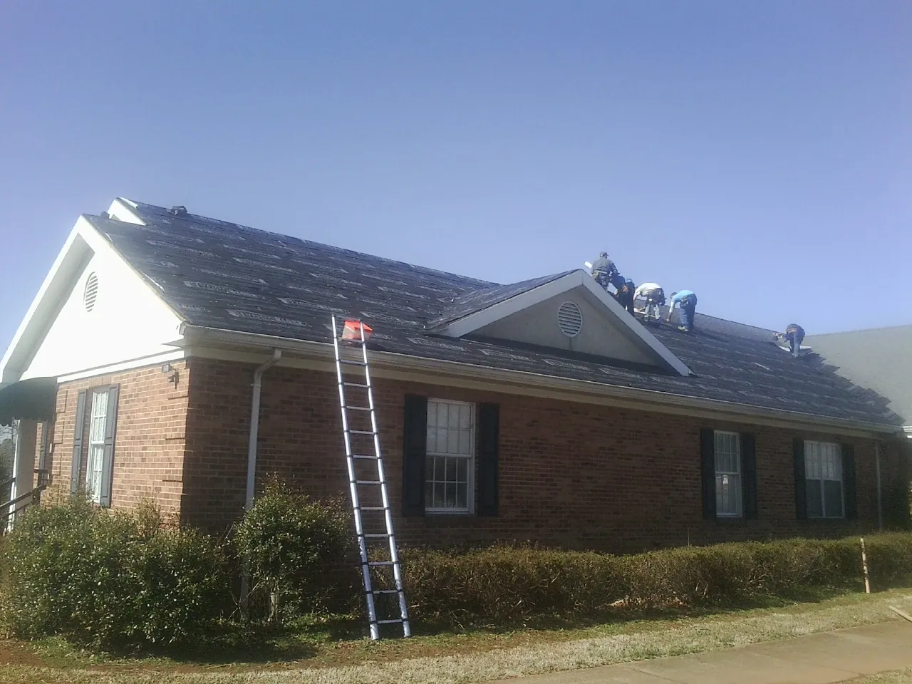 Crew tearing shingles off a brick ranch roof with a ladder set — Emergency Roof Repair work by our crew in State Center