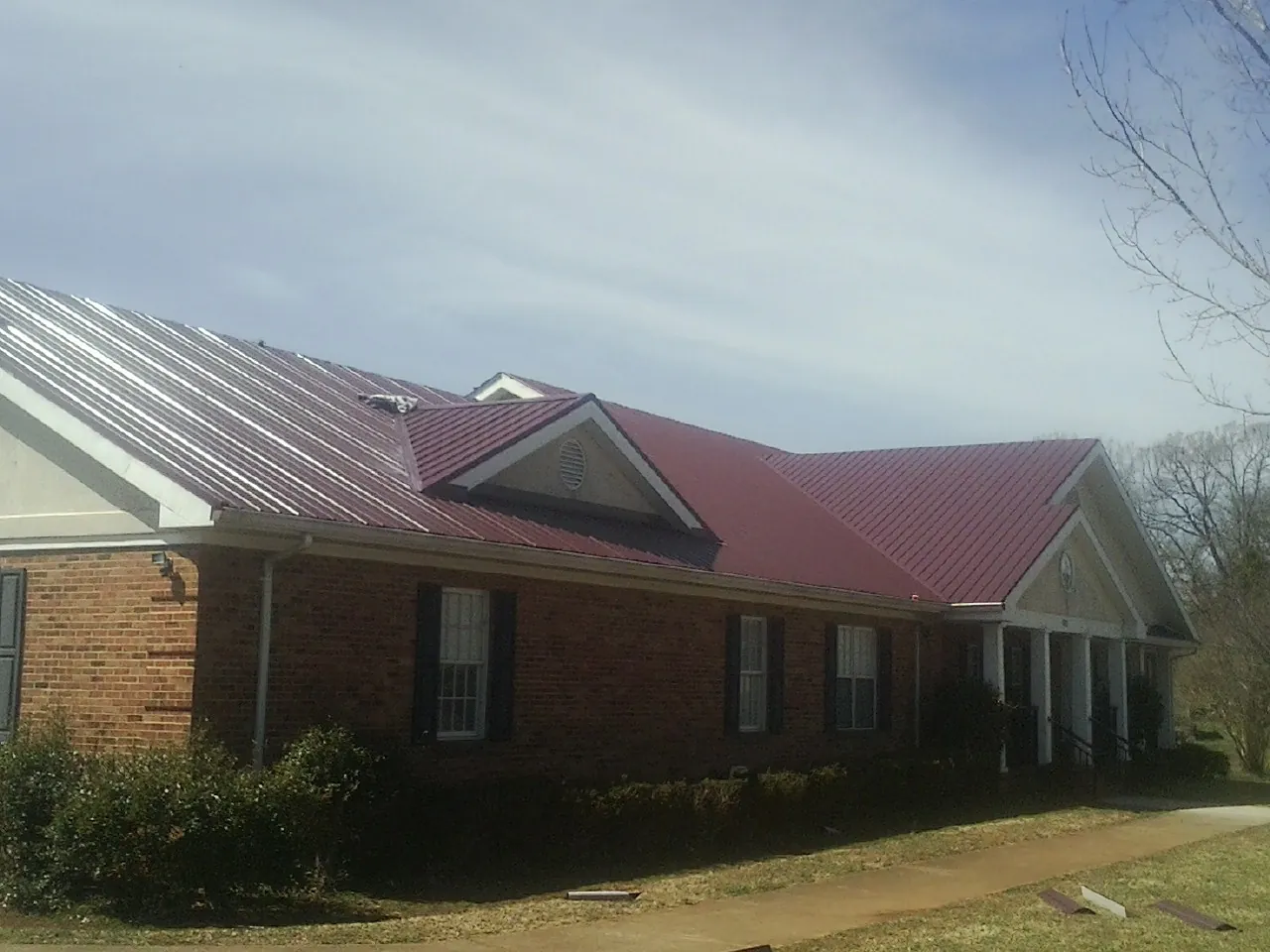 Red metal roof with gabled entries on a long brick building, from a Hail Damage Roof Repair job in State Center