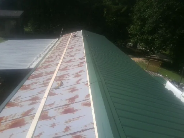 Old rusted panels beside newly installed green metal roofing — Wind Damage Roof Repair by Roofing Brothers in State Center