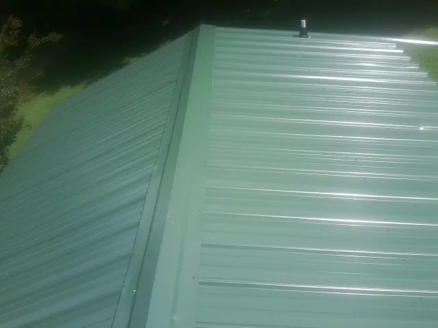 New green metal panels meeting at the ridge of a roof — Flat Roof Repair work by our crew in State Center