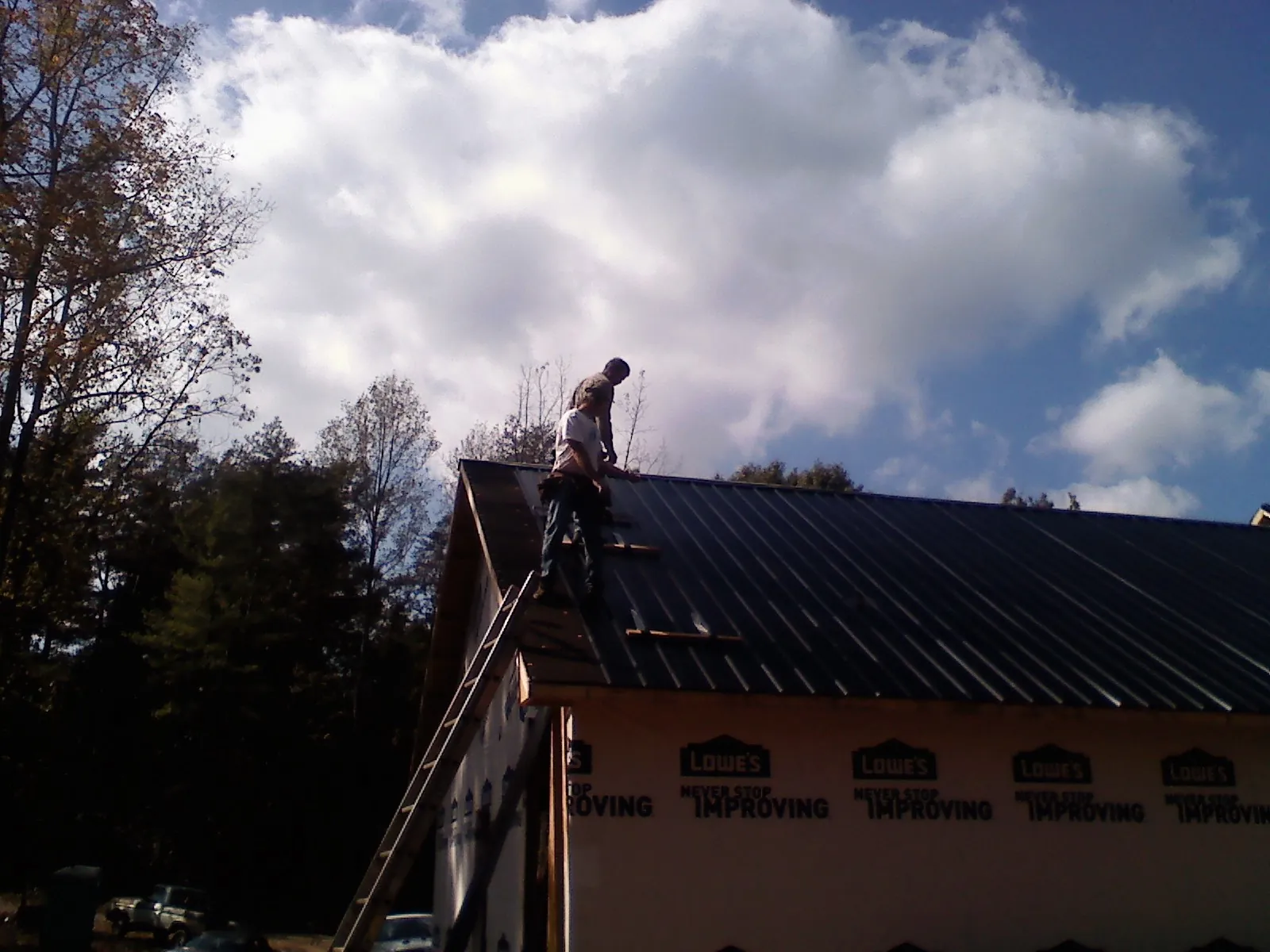 Roofer fastening dark metal panels high against a cloudy sky, from a Roof Inspection job in State Center