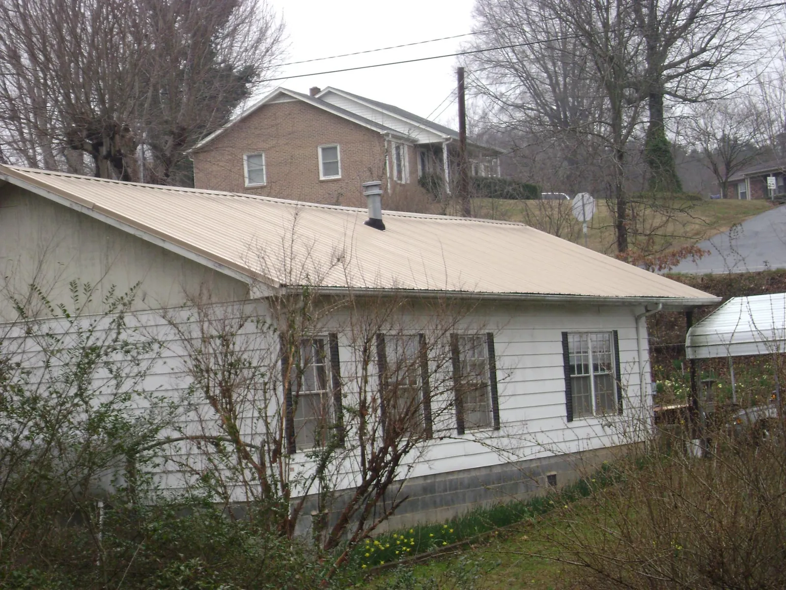 Tan metal roof on a white sided house set into a hillside — Commercial Roofing by Roofing Brothers in State Center