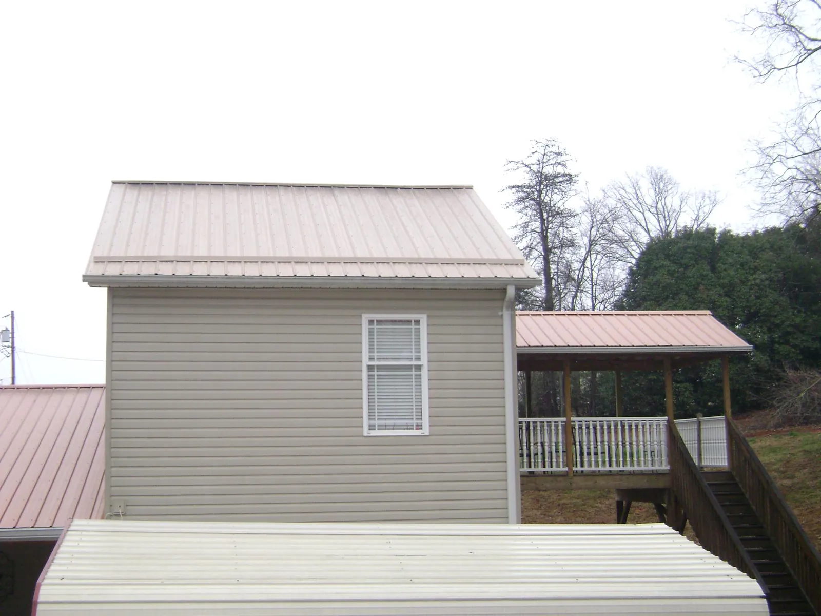Tan metal roofs on a two story addition and attached porch, from a Roof Replacement job in State Center